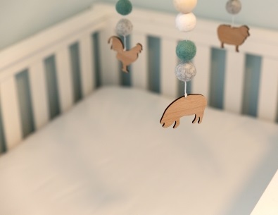 Close up of wooden pig on mobile hanging above white crib