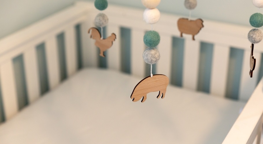 Close up of wooden pig on mobile hanging above white crib