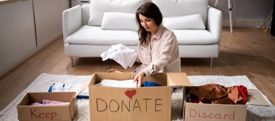 Person sitting on floor sorting items into three boxes labeled: keep, donate, discard