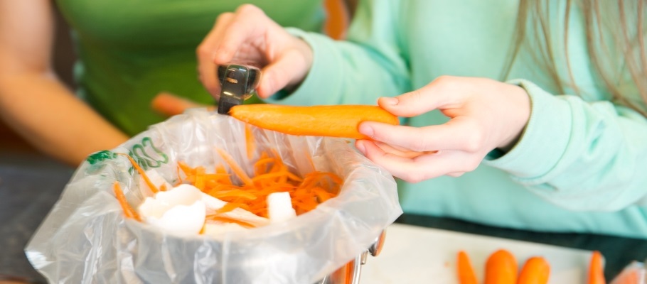 Child hands peeling carrots into organics bin on counter