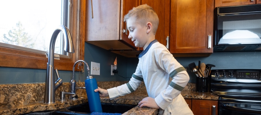Child filling reusable water bottle from the sink